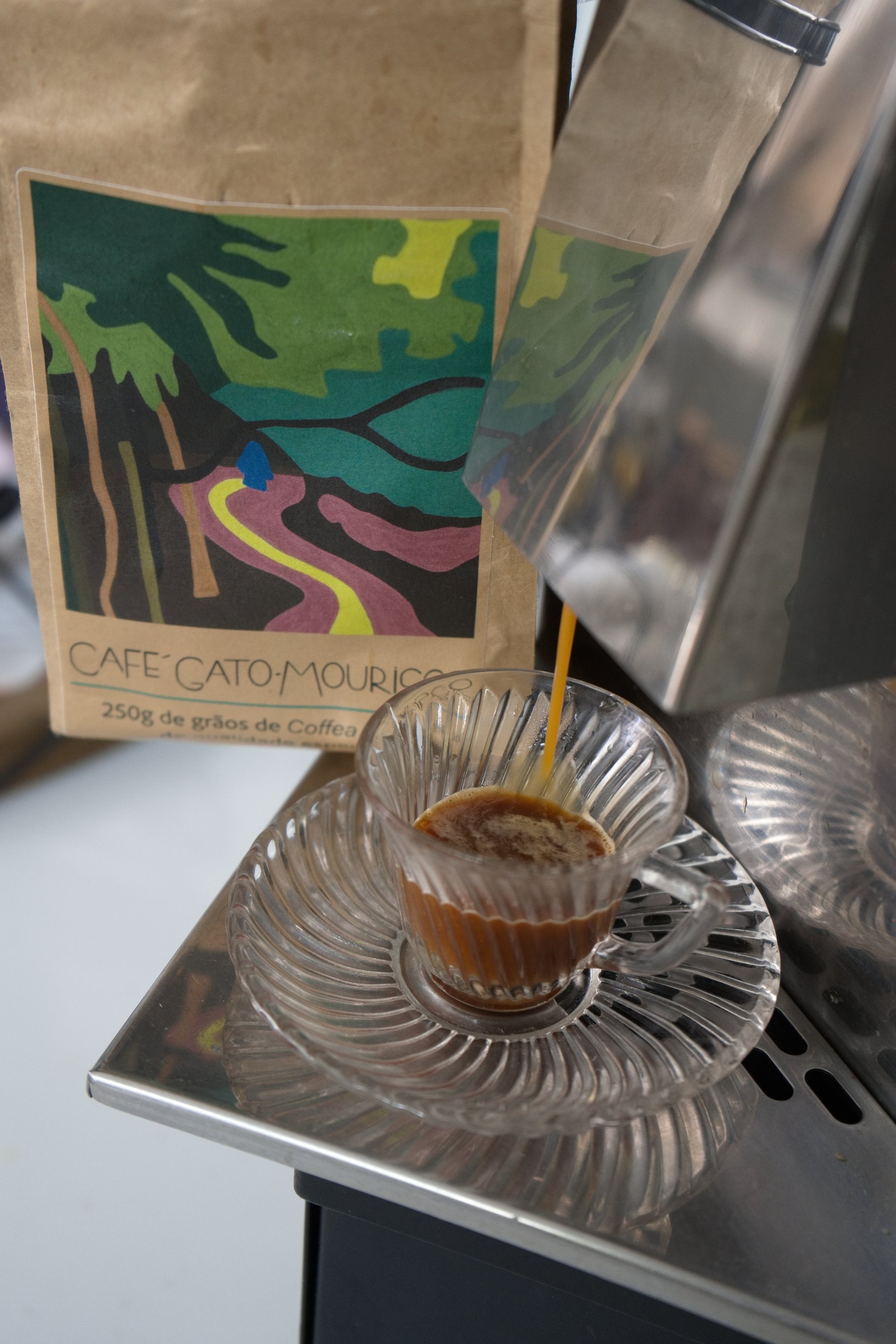 Embalagem do Café Gato-Mourisco ao lado de uma xícara de vidro durante a extração do espresso
